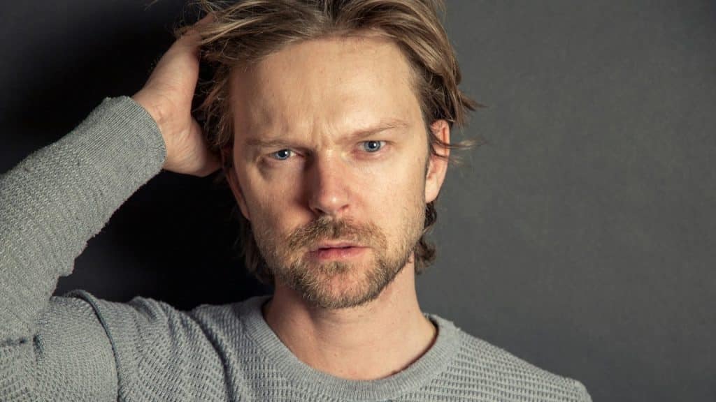 A lightly bearded man with an intense expression.