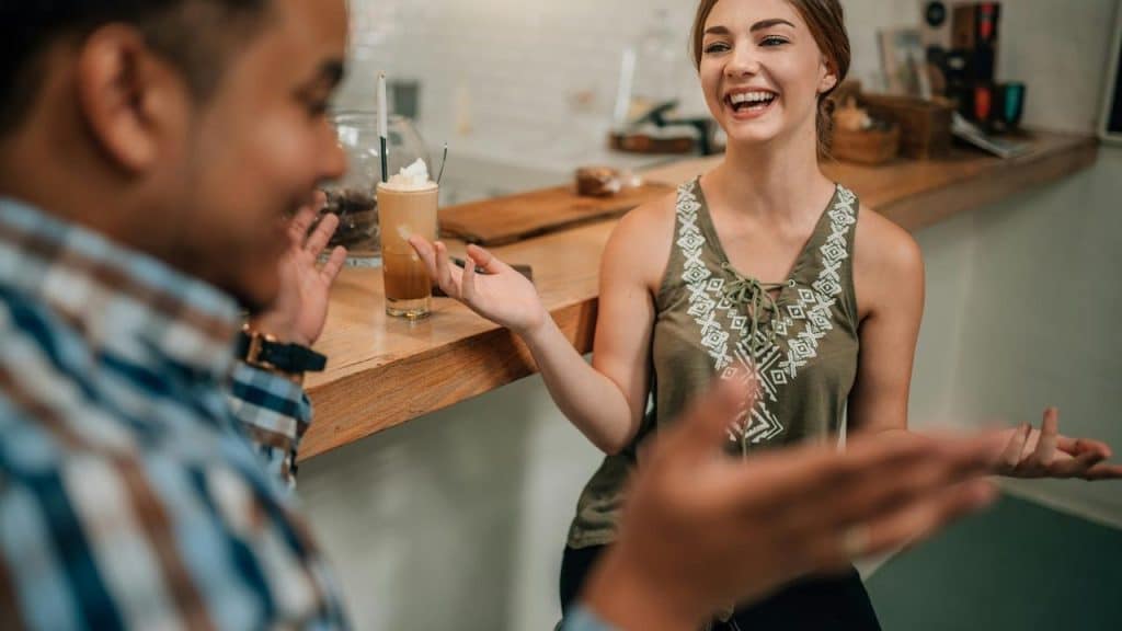 A woman laughing and gesturing to a man at a café counter.