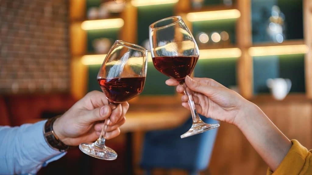 A close-up of two people cheering glasses filled with red wine.