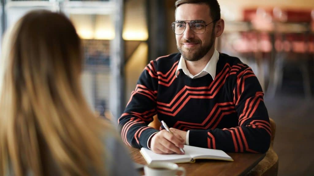 A man talking to a woman while writing on a notebook.