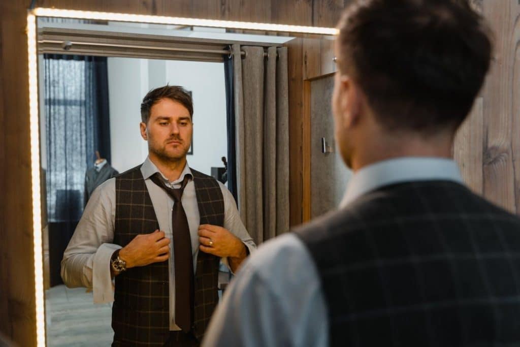 The man is in front of a mirror, checking his clothes.