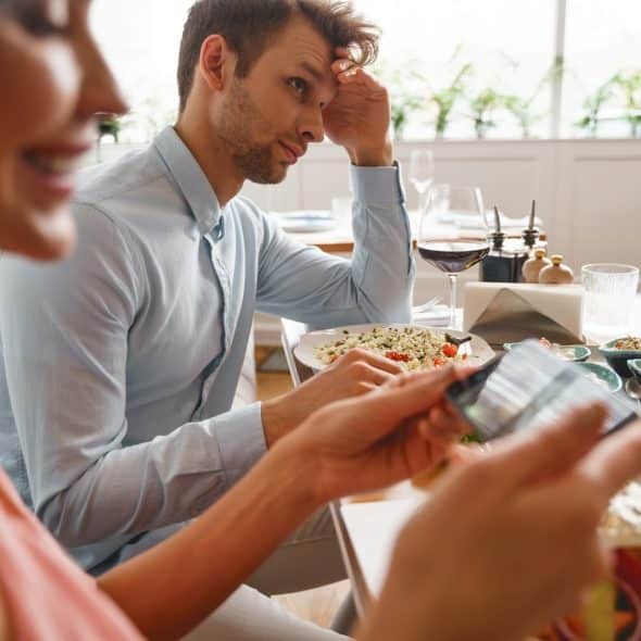 The man looks annoyed while the woman is taking photos of the food.