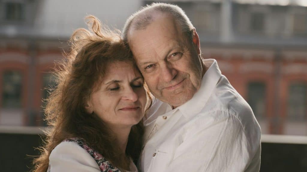 A close-up of a smiling, older, fair-skinned couple embracing outdoors.