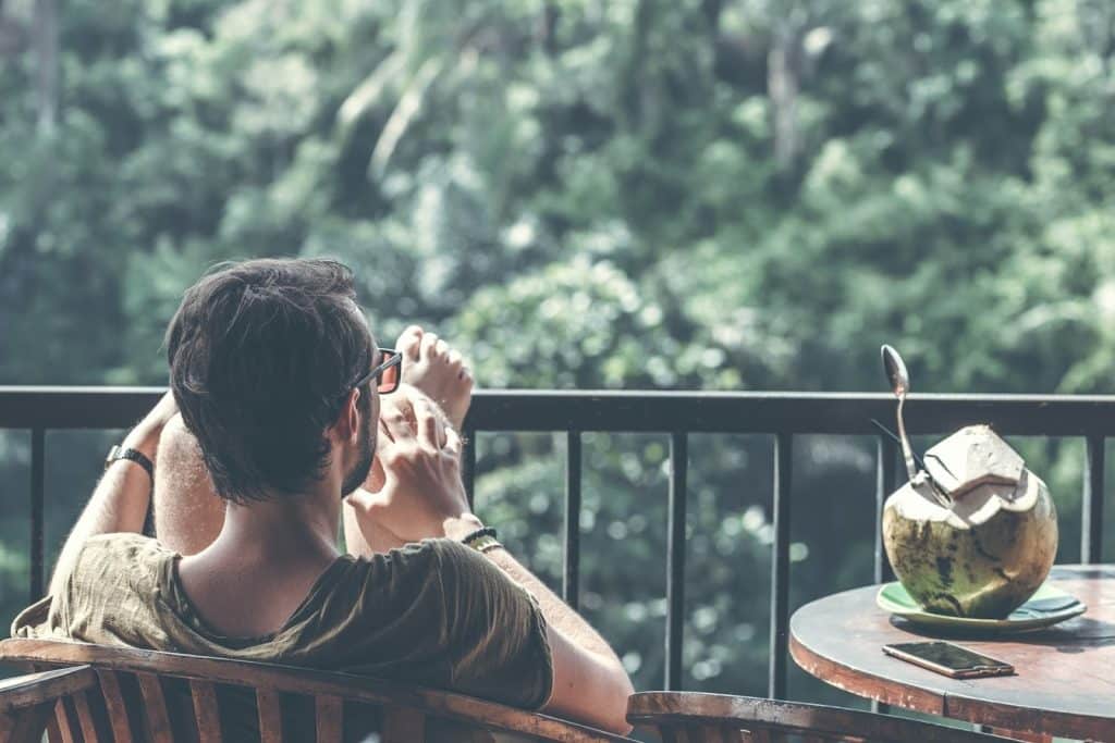 The man is sitting on an armchair, and the coconut is on the table beside him.