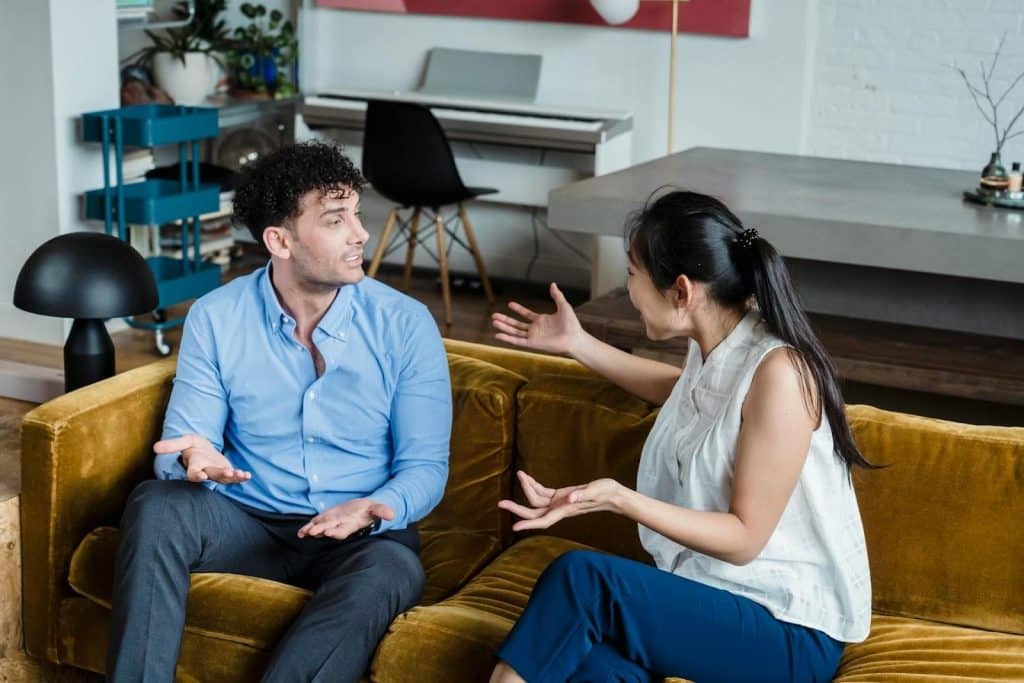 The couple is sitting on the couch and arguing.