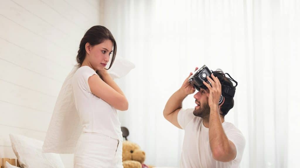 A woman in bed is about to start a pillow fight with her husband.