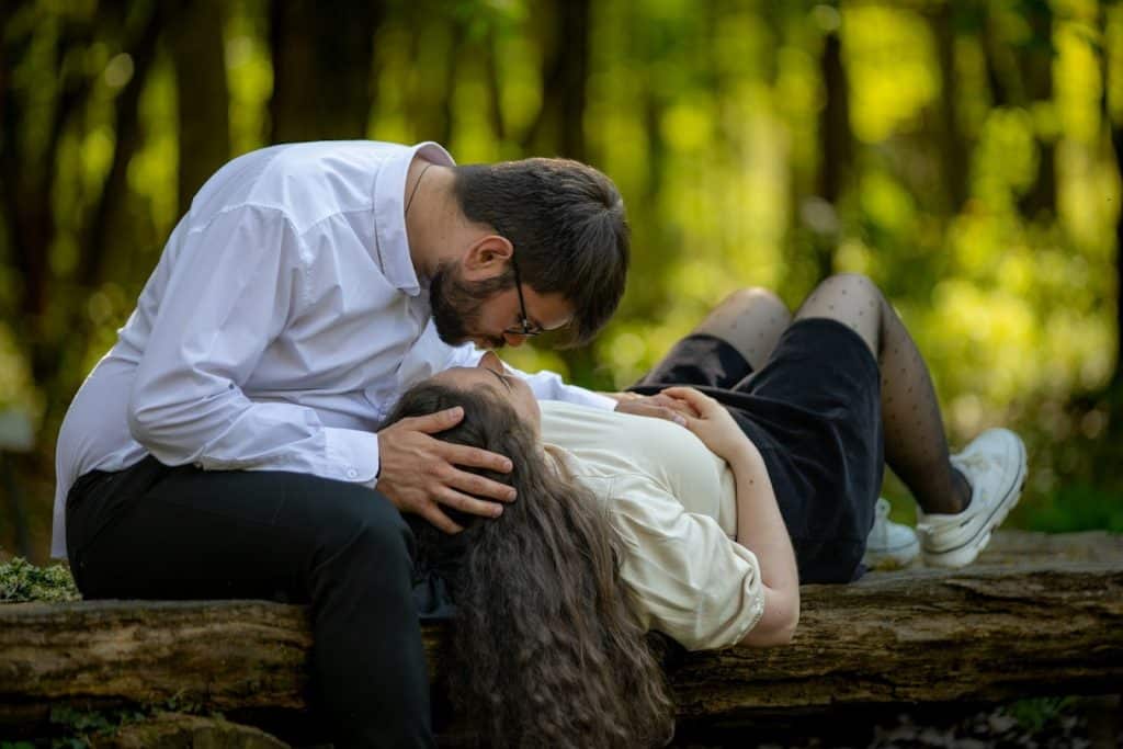 The couple is sitting on a log and are about to kiss.