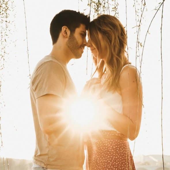 A man and woman holding hands while standing together at sunset.