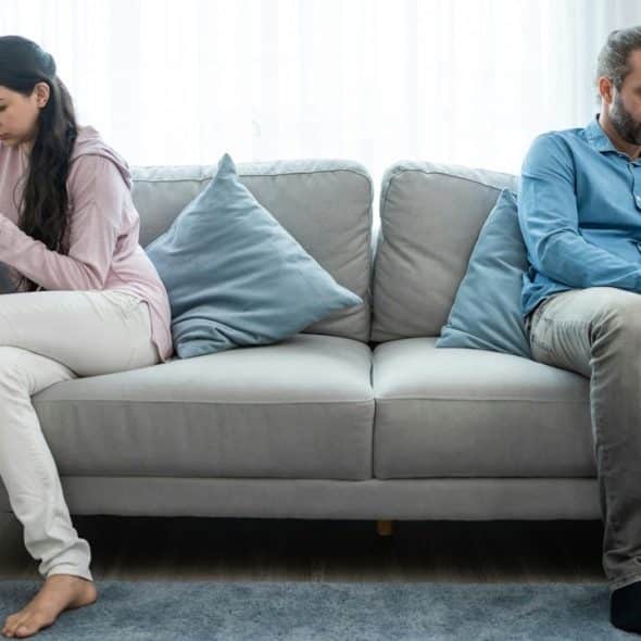 Couple sitting far apart on a couch, both looking at their phones, avoiding eye contact.
