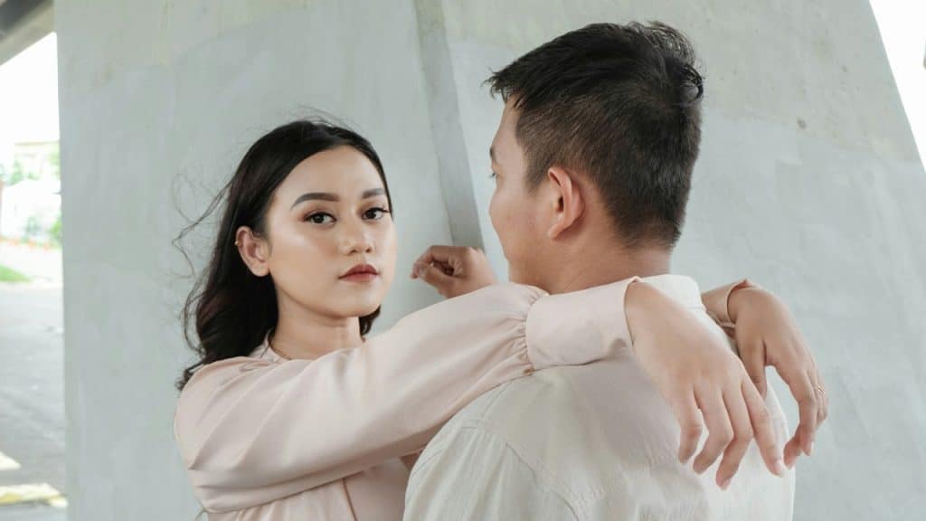 Couple embracing under a concrete structure, the woman looking directly at the camera.