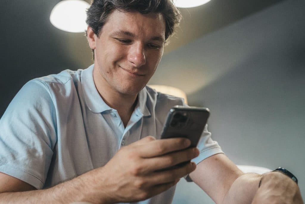 The man is smiling while texting.
