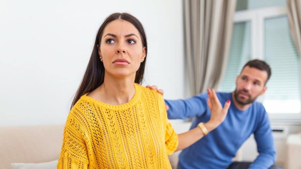 Woman in a yellow sweater rejecting a man's attempt to touch her shoulder.