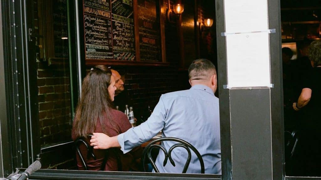 Couple sitting at a table inside a dimly lit restaurant, viewed through a window.