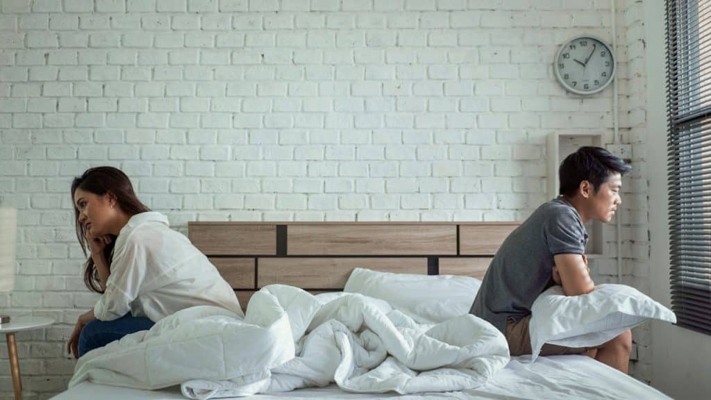 Couple sitting on the edge of a bed, turning away from each other after an argument.