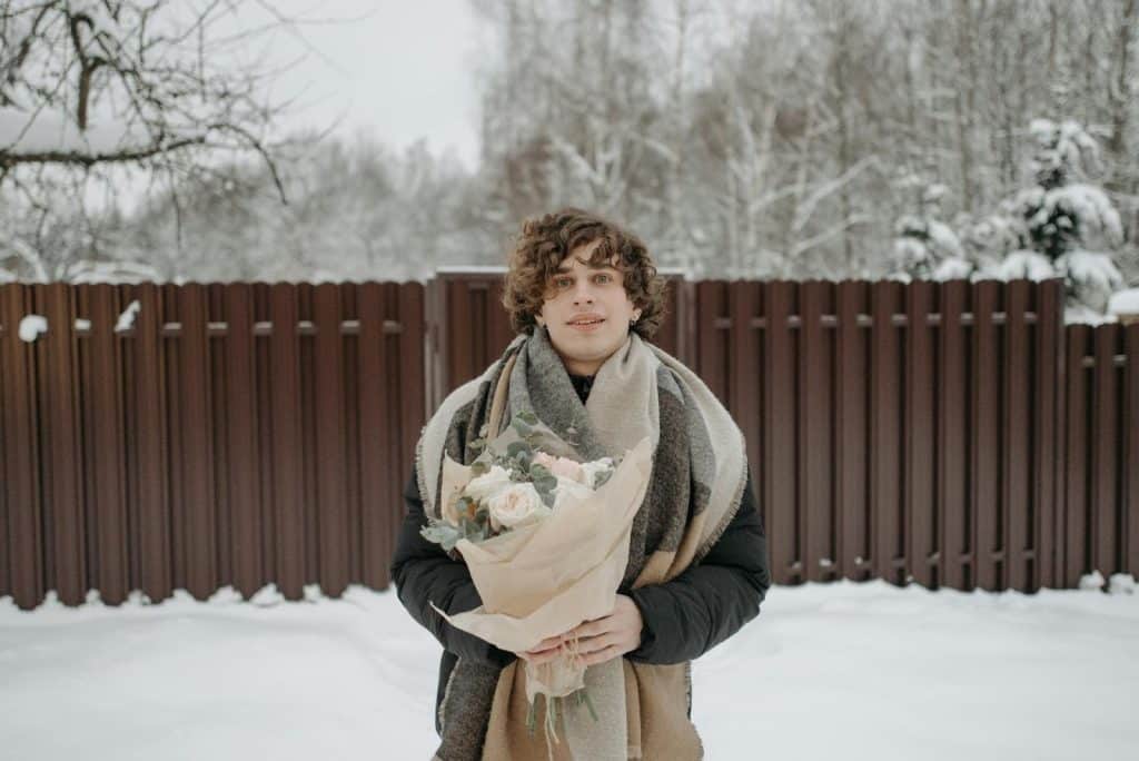 The man is holding a bouquet of flowers out in the snow.