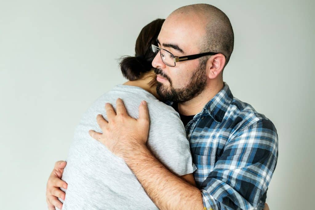 The man in a plaid shirt is hugging the woman.