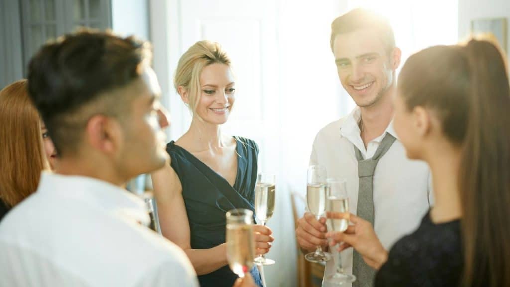 Four people smiling and holding champagne flutes at a brightly lit social gathering.