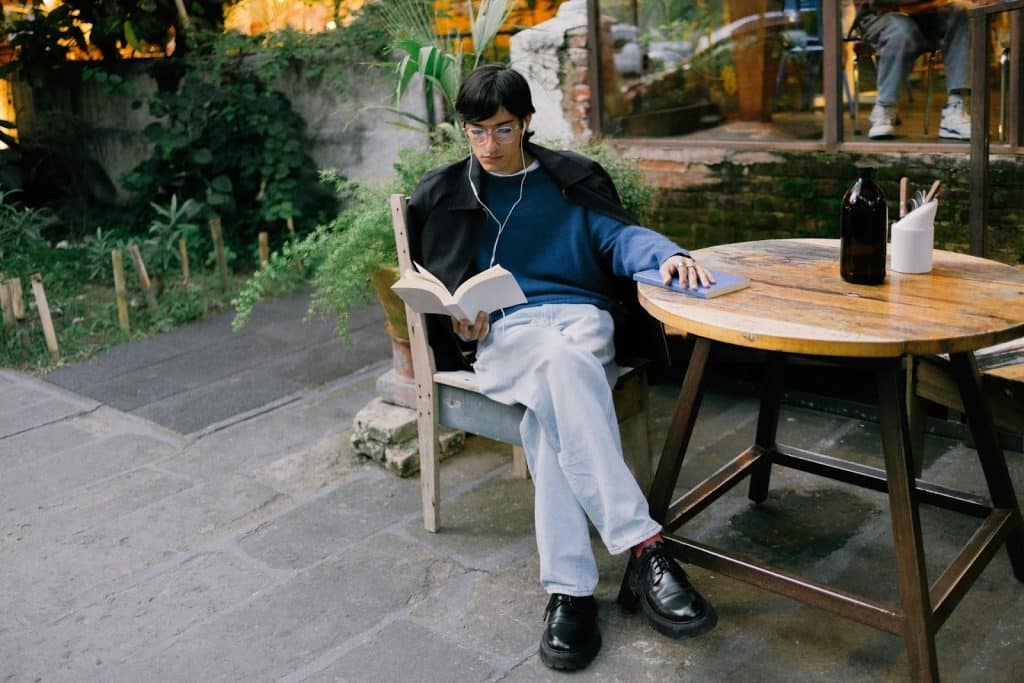 The man is reading a book outside the café.