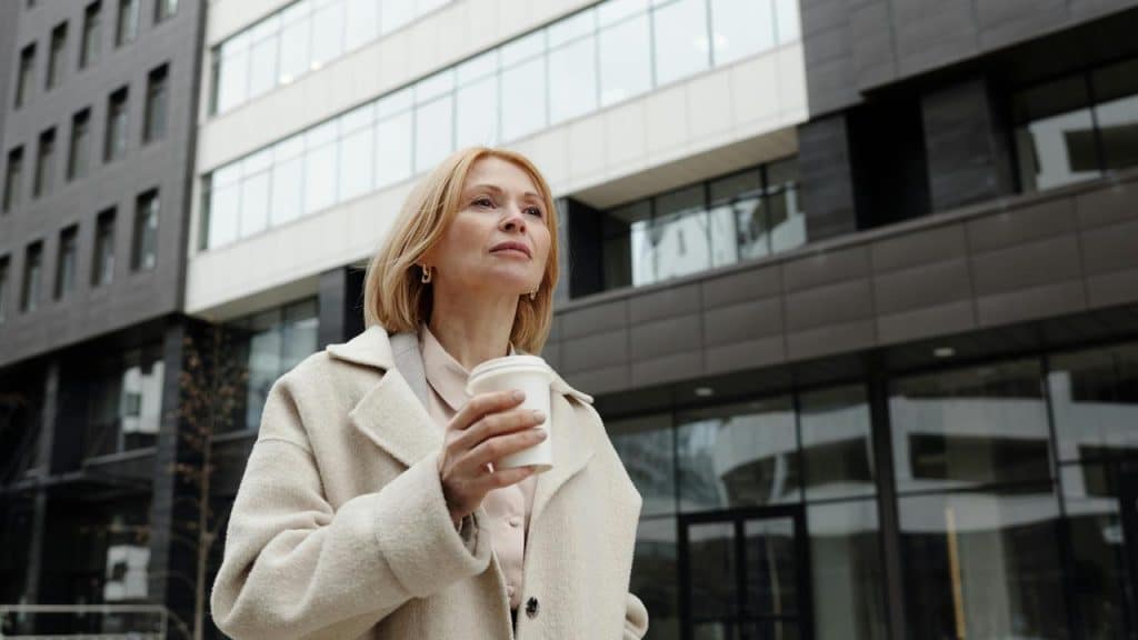 A woman stands outside a modern building holding a takeaway coffee cup.