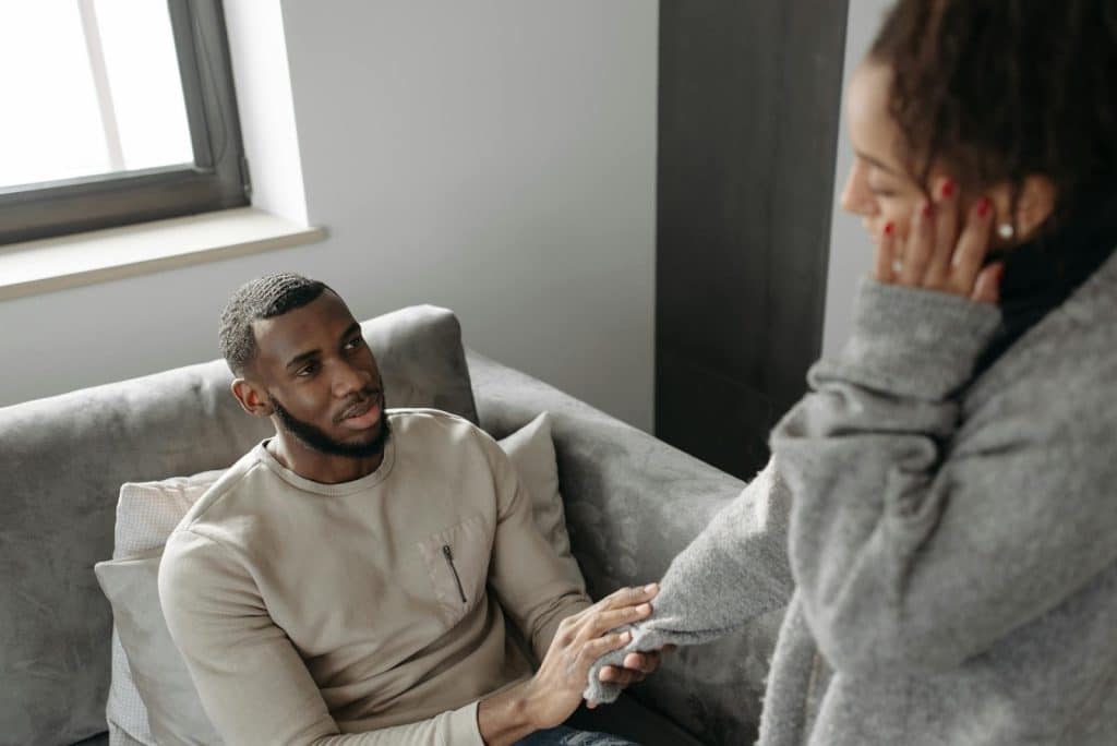 A man sitting on the couch is holding the woman’s hand.