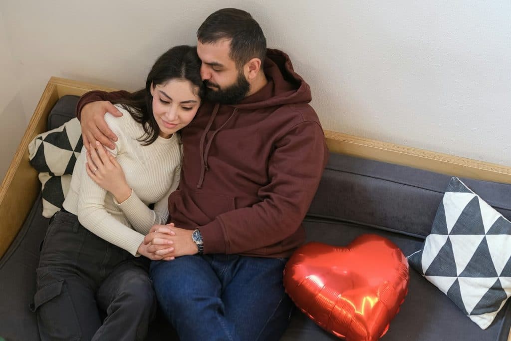 A man and woman hugging each other while sitting on a couch.