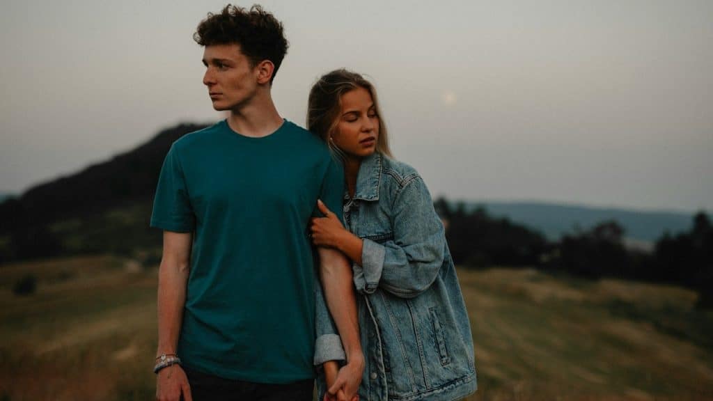 A couple holding hands but looking away from each other.