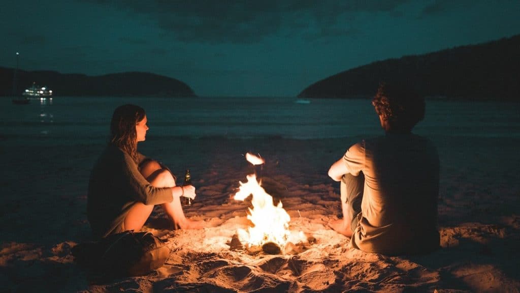 Man and woman with bone fire sitting on seashore.