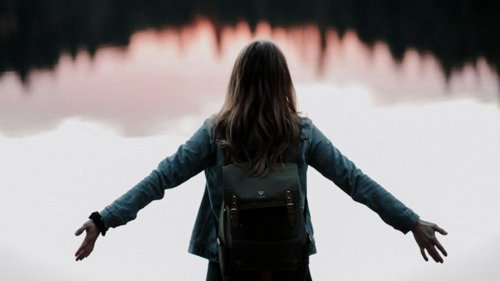 A woman standing with her arms stretched in front of a body of water.