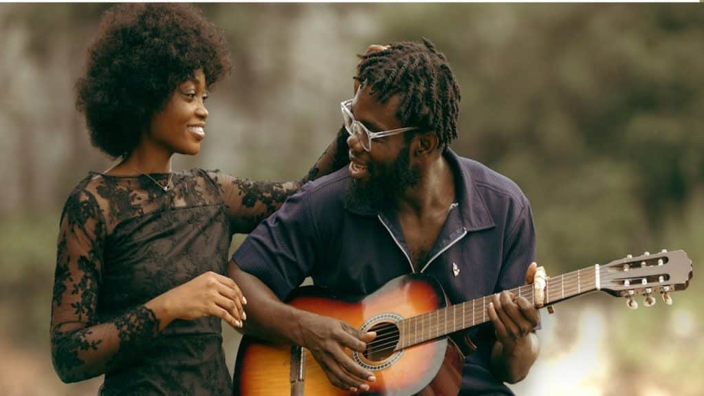 A woman stroking the hair of a man who’s playing a guitar.