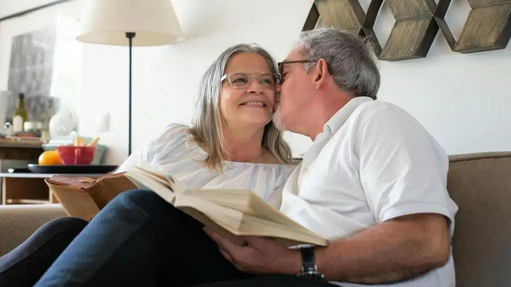 A couple sitting on a couch reading as the man kisses the woman’s cheek.Marriage starts feeling like a never-ending rerun when the surprises run out. Predictability might feel cozy, but too much of it makes life feel.. bland.