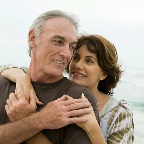 A couple holding each other close while standing on a beach.