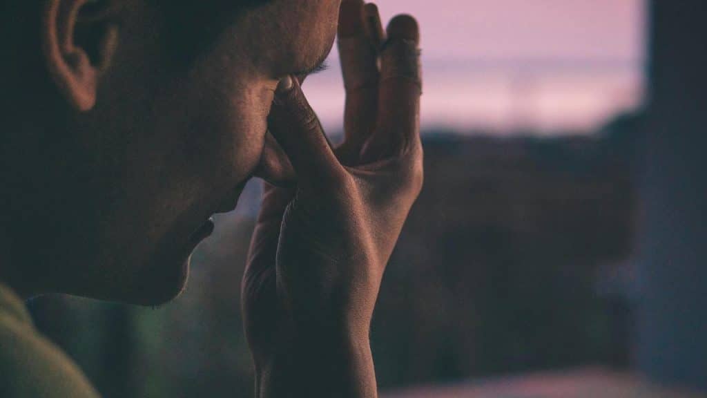 A close-up of a person touching their face with a tired or stressed expression.