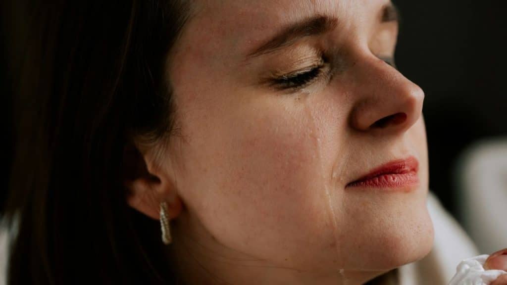 A close-up of a woman's face, eyes closed, with a tear running down her cheek.