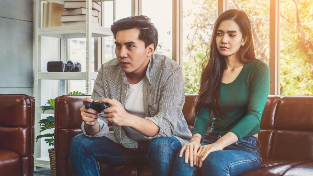 Man focuses on a video game controller while a woman sits next to him looking annoyed.
