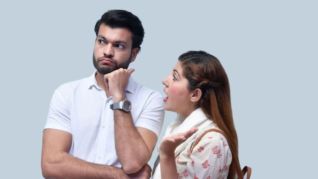 Man with a beard looks away scornfully while a woman talks animatedly with an open mouth.