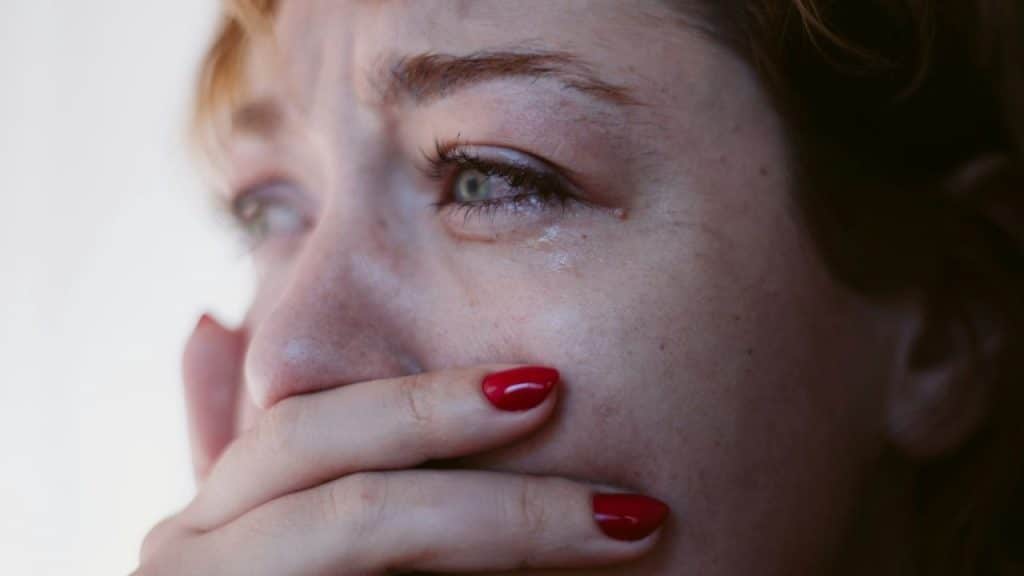 A close-up of a woman crying with a tear on her cheek and her hand over her mouth.
