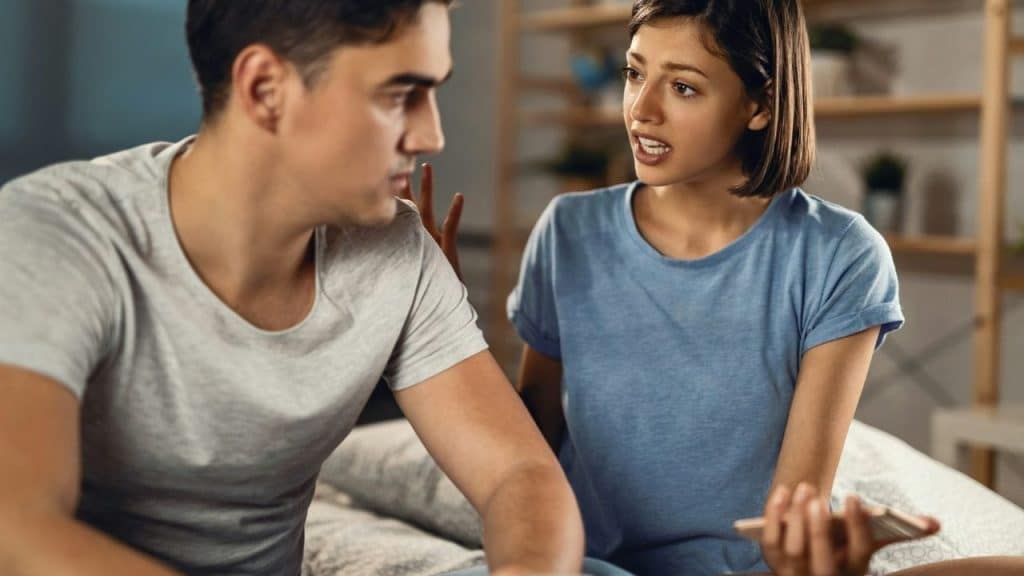 A distressed woman holding a phone speaks to a man who looks away from her.