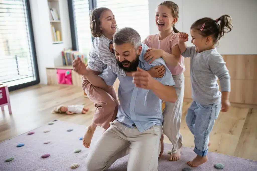 A father playing with three daughters at home.