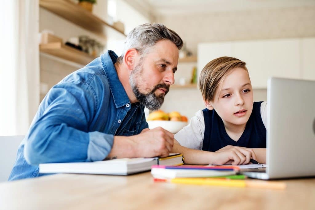A mature dad sitting with son at a table at home.