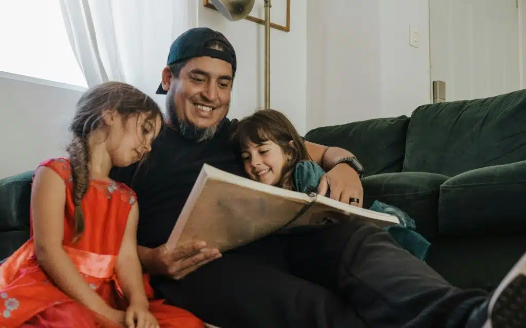 A father reading a book with two daughters.
