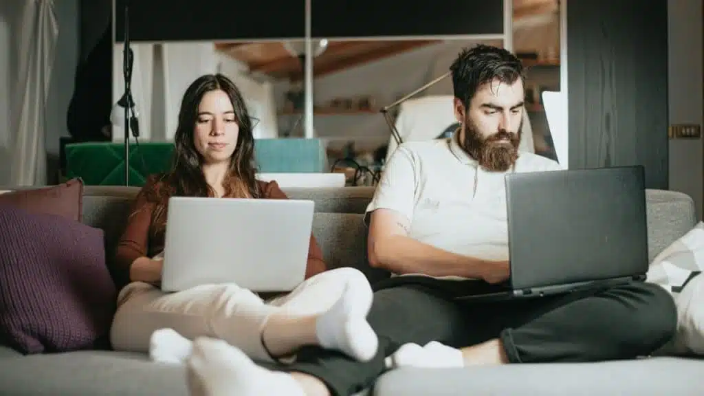 Man and woman sitting on a couch working on separate laptops.