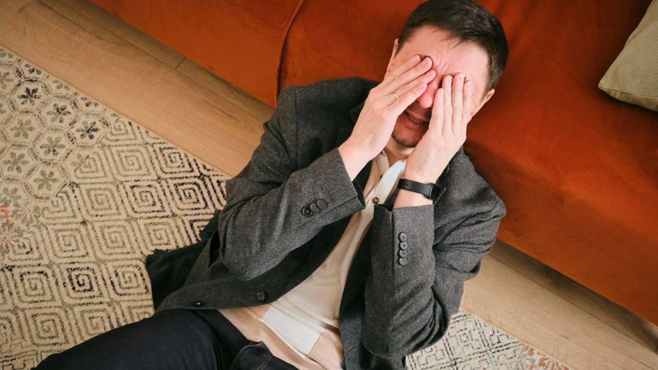 Man lying on the floor covers his face with his hands in distress.
