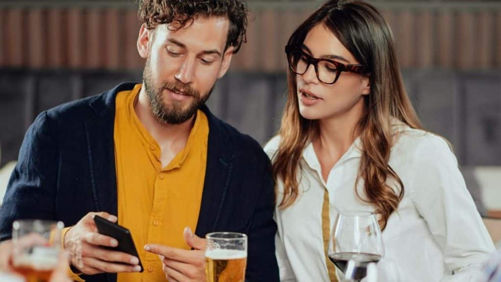 A man and woman seated at a table look at a phone together.