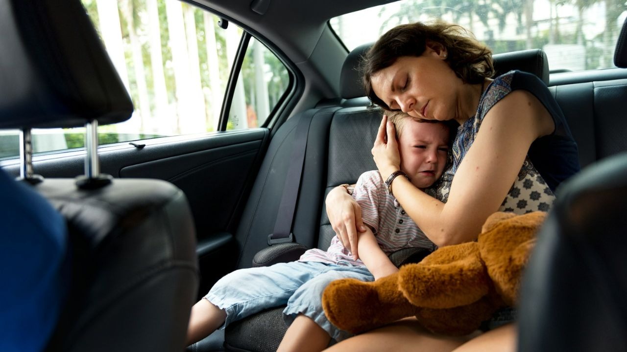 Mother embracing a young, crying child in the backseat of a car.