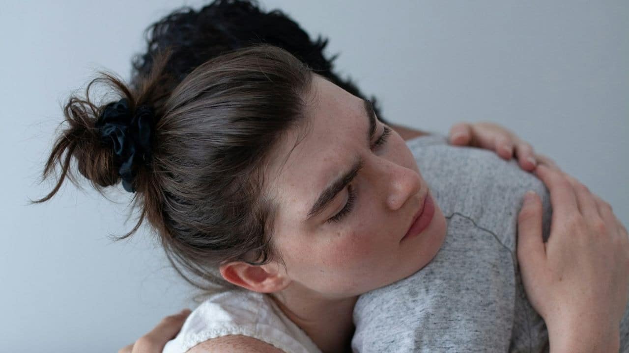 A woman with her eyes closed is hugging another person in a gray shirt.