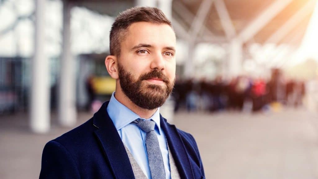 Portrait of a bearded man in a suit jacket, tie, and shirt outdoors.