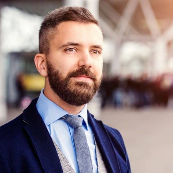 Portrait of a bearded man in a suit jacket, tie, and shirt outdoors.