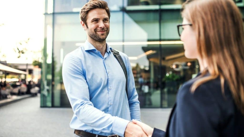 Two people in professional attire are shaking hands outside a modern building.