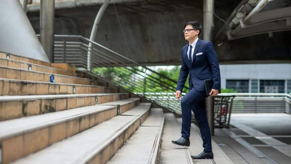 Man in a dark suit ascending a wide outdoor staircase holding a tablet.