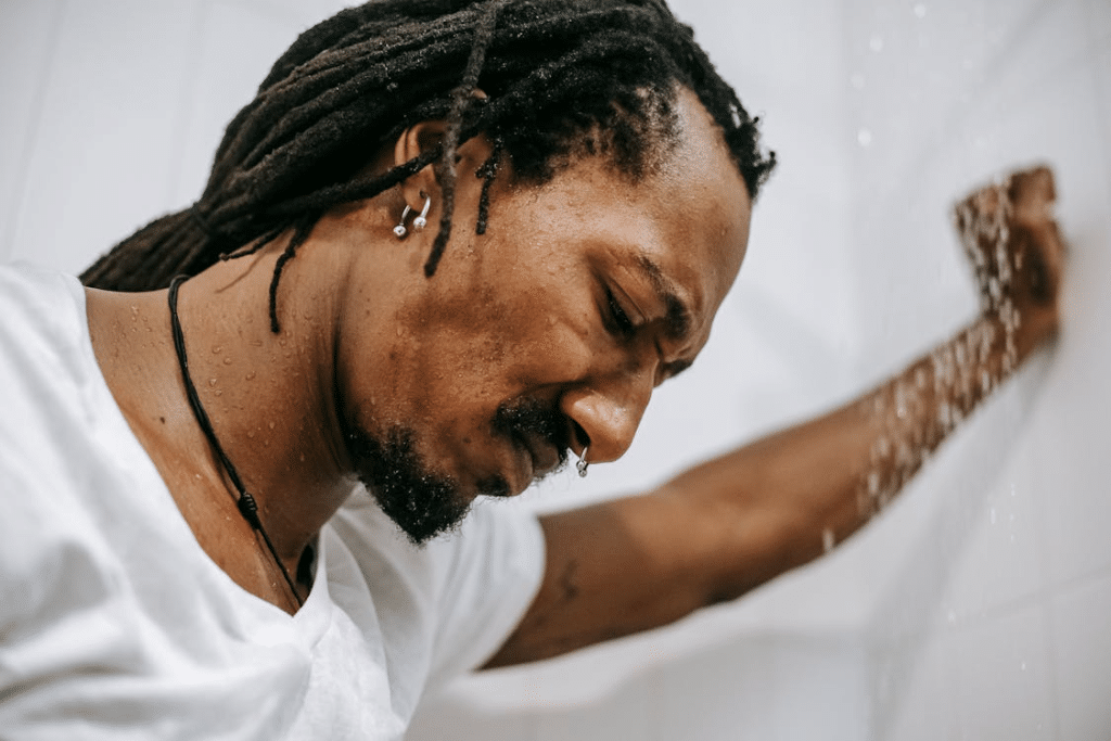 Crop frustrated black man standing in shower cabin